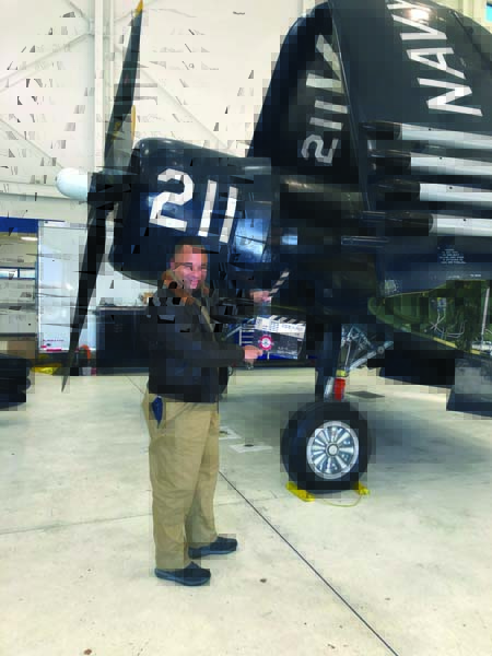  Mike Oliver poses with a director’s action/cut clapper board in front of Erickson Aircraft Museum’s Corsair, the “hero” aircraft in “Devotion.” (Photo courtesy Mike Oliver)